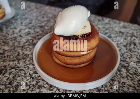Primo piano di un dessert gourmet con un'alta pila di pancake spessi e soffici. La pila si trova in una piscina di sciroppo d'acero ed è ricoperta di cioccolato Foto Stock