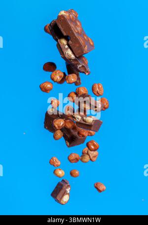 Pezzi di cioccolato con noci cadono nell'aria su uno sfondo blu brillante in uno scatto ad alta velocità catturando movimento e scricchiolio Foto Stock