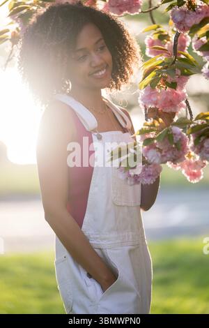 Una giovane donna afroamericana con capelli ricci sorride alla telecamera. Foto Stock