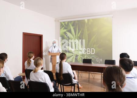 Professionista del settore sanitario che tiene una lezione sul CBD nella sala conferenze utilizzando un videoproiettore. Illustrazione sullo schermo di proiezione Foto Stock