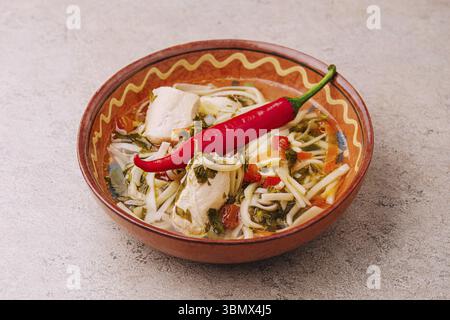 Natura morta alimentare, zuppa di pollo - brodo con spaghetti, erbe, pepe e verdure sul piatto Foto Stock