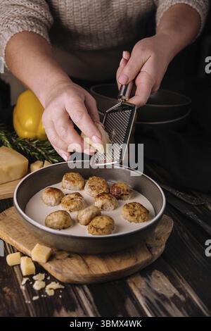 Cibo natura morta, donna che grattugia il parmigiano sulle polpette in salsa panna Foto Stock