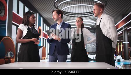 Il manager ha pianificato una strategia con un team eterogeneo davanti a un caffè nel concierge del ristorante alla moda che si è messo in contatto con il personale dell'hotel su tablet Foto Stock