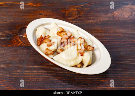 Deliziosi gnocchi ripieni di patate e formaggio ricoperti di pancetta croccante sono presentati in un piatto bianco su un rustico tavolo di legno, invitante a un richiamo Foto Stock