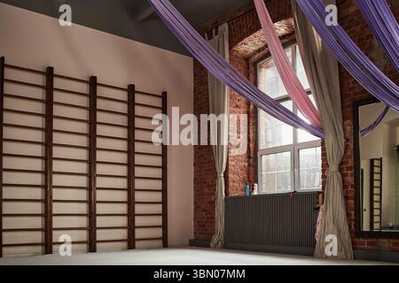 Studio di ginnastica ritmica vuoto con barre a parete e nastri in tessuto sospesi appesi al soffitto, grande finestra che consente la luce naturale e specchio che riflette parte della stanza Foto Stock