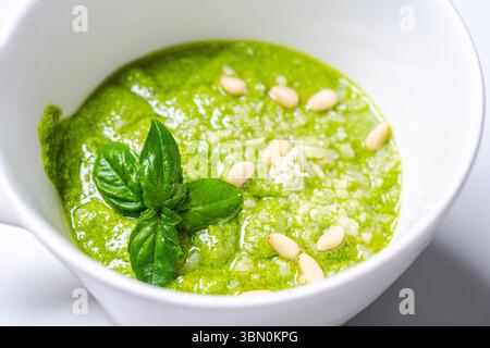 Salsa al pesto secondo una tradizionale ricetta italiana in una casseruola su sfondo bianco, decorata con basilico e pinoli. Foto di alta qualità Foto Stock