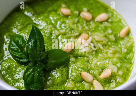 Salsa al pesto secondo una tradizionale ricetta italiana in una casseruola su sfondo bianco, decorata con basilico e pinoli. Foto di alta qualità Foto Stock