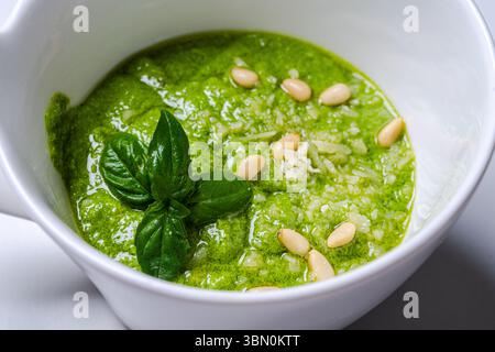 Salsa al pesto secondo una tradizionale ricetta italiana in una casseruola su sfondo bianco, decorata con basilico e pinoli. Foto di alta qualità Foto Stock