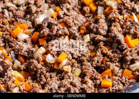 Il manzo macinato con carote, cipolle e sedano viene fritto per preparare una salsa alla bolognese secondo una tradizionale ricetta italiana. Sfondo. Vista dall'alto. Foto Stock