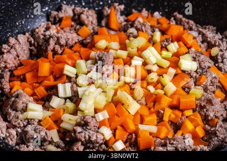 Il manzo macinato con carote, cipolle e sedano viene fritto per preparare una salsa alla bolognese secondo una tradizionale ricetta italiana. Sfondo. Vista dall'alto. Foto Stock