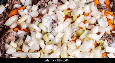 Il manzo macinato con carote, cipolle e sedano viene fritto per preparare una salsa alla bolognese secondo una tradizionale ricetta italiana. Sfondo. Vista dall'alto. Foto Stock