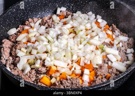 Il manzo macinato con carote, cipolle e sedano viene fritto per preparare una salsa alla bolognese secondo una tradizionale ricetta italiana. Sfondo. Vista dall'alto. Foto Stock