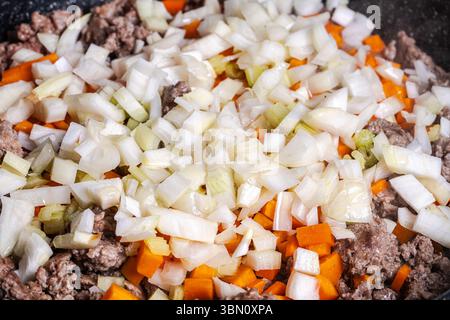 Il manzo macinato con carote, cipolle e sedano viene fritto per preparare una salsa alla bolognese secondo una tradizionale ricetta italiana. Sfondo. Vista dall'alto. Foto Stock