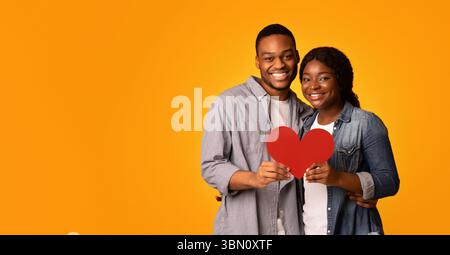 Gioiosa coppia nera amorevole che tiene insieme il cuore di carta rossa e. Agguato Foto Stock