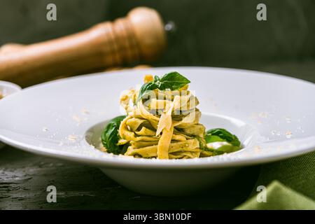 Fituccine con pesto di basilico e pinoli su un piatto bianco con forchetta. Fituccine al pesto secondo una ricetta tradizionale italiana. Q. Alta Foto Stock