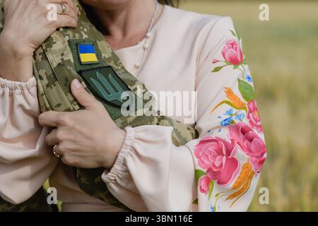 Primo piano di una donna con un tradizionale abito ricamato ucraino che abbraccia un soldato in uniforme mimetica con bandiera e toppa tridente, mostrando emozione Foto Stock