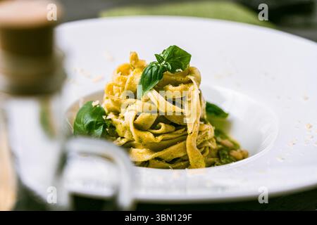 Fituccine con pesto di basilico e pinoli su un piatto bianco con forchetta. Fituccine al pesto secondo una ricetta tradizionale italiana. Q. Alta Foto Stock