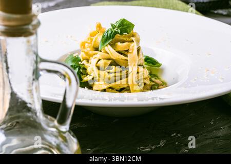 Fituccine con pesto di basilico e pinoli su un piatto bianco con forchetta. Fituccine al pesto secondo una ricetta tradizionale italiana. Q. Alta Foto Stock