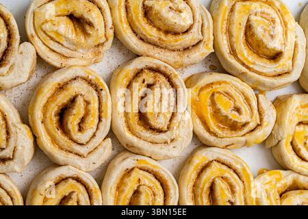 Preparare focaccine di pasta sfoglia alla cannella fatte in casa. Rotoli di impasto crudi ingrassati con tuorlo d'uovo. Foto di alta qualità Foto Stock