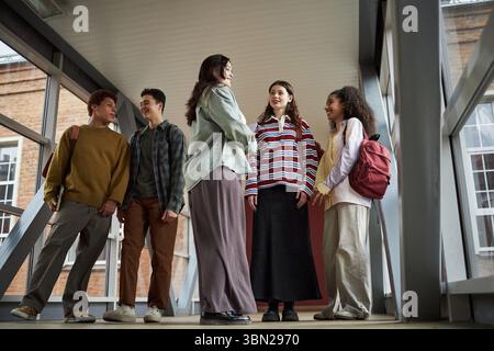 Gruppo di studenti universitari multietnici in corridoio che parlano e sorridono, giovani uomini e donne adulti che interagiscono insieme, conversazione informale durante le pause tra le lezioni Foto Stock