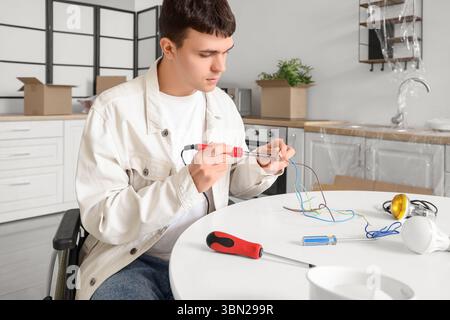 Giovane uomo in sedia a rotelle che ripara la lampada sul tavolo a casa Foto Stock