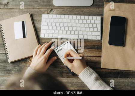 Draufsicht auf eine Frau, Die in ein Notizbuch Plaene fuer die Arbeitswoche am Arbeitsplatz schreibt Foto Stock