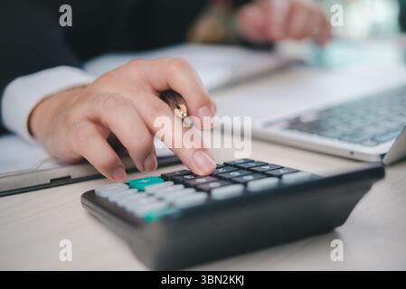 Uomo d'affari che calcola i dati finanziari con calcolatrice e laptop. Pianificazione del bilancio e analisi finanziaria per contabilità, deposito fiscale e operazioni di pronti contro termine finanziarie Foto Stock