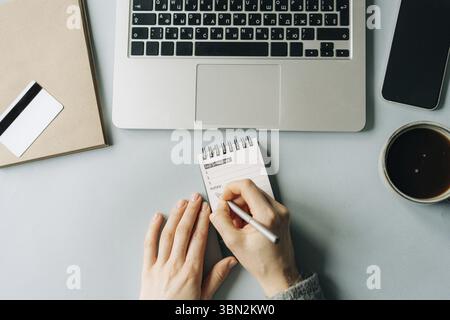 Draufsicht auf eine nicht erkennbare Frau, die auf einem Buerotisch arbeitet und Ziele in Notizen schreibt Foto Stock