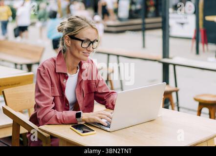 Giovane donna caucasica attraente seduta in un caffè lavora su un computer portatile Foto Stock