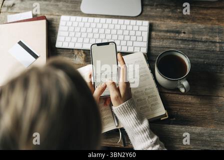 Draufsicht auf eine Frau, Die am Arbeitsplatz im Buero Notizen in das Telefon schreibt Foto Stock