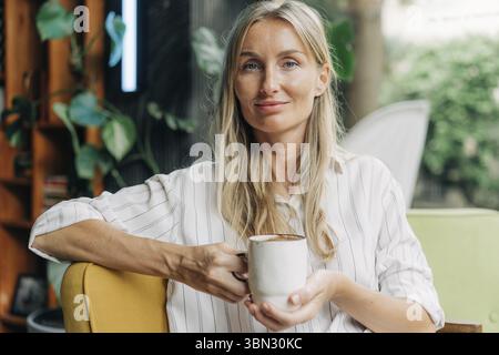 Ritratto testimoniale di una giovane donna con una tazza di caffè seduta in una moderna caffetteria Foto Stock