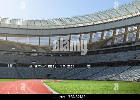 Lo stadio di atletica presenta una pista da running rossa dal design piatto, erba verde, tabellone segnapunti e capriate in acciaio Foto Stock