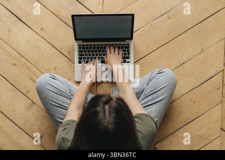 Draufsicht auf eine nicht zu erkennende Frau, die auf dem Boden sitzend an einem laptop arbeitet Foto Stock