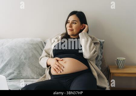 Incinta donna attraente siede sul divano in piacere Foto Stock