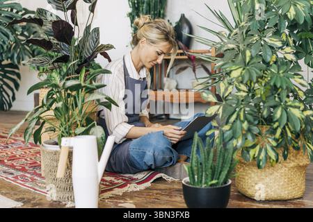 Geschaeftsfrau, Inhaberin eines Blumenstudios, sitzt auf dem Boden und arbeitet an einem Lapto Foto Stock