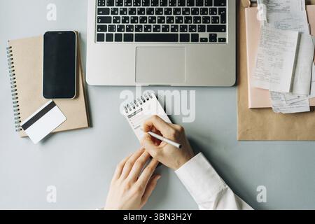 Draufsicht auf eine nicht erkennbare Frau, die auf einem Buerotisch arbeitet und Ziele in Notizen schreibt Foto Stock