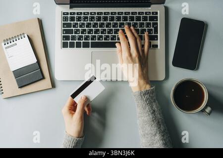 Draufsicht auf eine nicht erkennbare Frau, Die an einem laptop arbeitet und eine Kreditkarte fuer die Online-Zahlung haelt Foto Stock