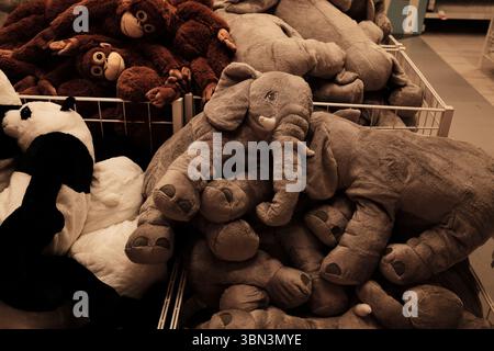 Una pila di elefanti, panda e scimmie di peluche esposti in un cestino di metallo in un negozio di giocattoli. Animali morbidi e soffici farciti messi in vendita. Foto Stock