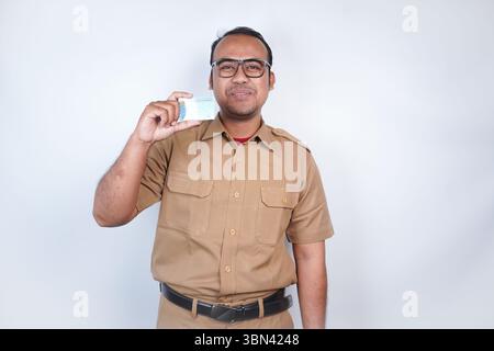 Un uomo funzionari pubblici asiatici o funzionari statali è con l'uniforme marrone. Gesti con carta d'identità . Su sfondo bianco. Indonesia PNS, ASN Foto Stock