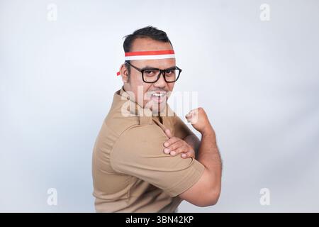 Un uomo funzionari pubblici asiatici o funzionari statali è con uniforme marrone e un gesto di fascia rossa e bianca che mostra un gesto forte sollevando le braccia Foto Stock