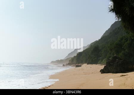 Spiaggia tropicale incontaminata con onde e lussureggianti scogliere verdi Foto Stock