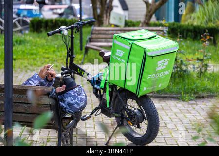 Foodini fattorino disteso su una panchina consultando il suo telefono Foto Stock