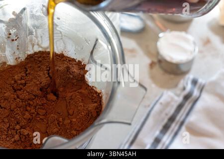 Sciroppo d'acero versato sul cacao, sulle uova e sull'impasto nel vaso frullatore Foto Stock