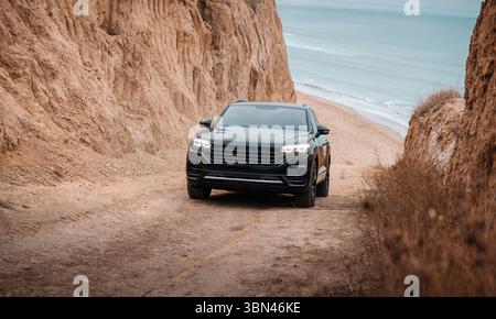 SUV nero in salita da una spiaggia vicino a una scogliera. SUV sportivo su una strada sterrata con terreno sabbioso vicino a un mare. Foto Stock