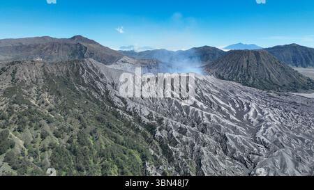 Un impressionante colpo di droni cattura le aspre pendici di un vulcano attivo con il fumo che sale dal suo cratere. Contrasto sorprendente tra le coperte di cenere Foto Stock