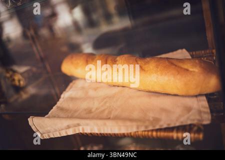 La baguette marrone dorato si trova su un panno in una vetrina da forno, invitando i clienti con il suo delizioso aroma e la crosta croccante Foto Stock