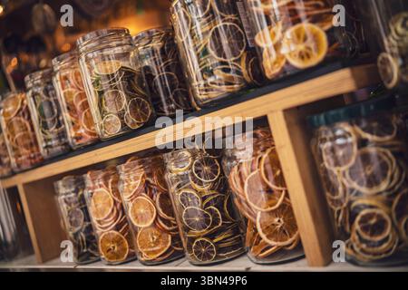 Varie fette di agrumi secchi, tra cui arance, limoni e pompelmo, sono disposte in barattoli di vetro su scaffali di legno, creando una visuale Foto Stock