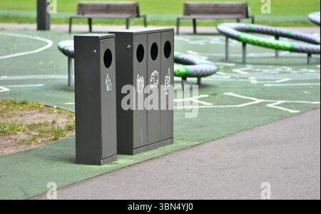 Lo smistamento dei contenitori dei rifiuti in un parco pubblico con contenitori separati per plastica, carta, vetro e rifiuti generici promuove la sostenibilità e la responsabilità Foto Stock