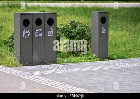 Smistamento dei contenitori dei rifiuti in un parco pubblico con contenitori separati per plastica, carta e vetro a sinistra e rifiuti generici a destra. Contrassegno di messa a terra Foto Stock