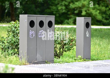 Smistamento dei contenitori dei rifiuti in un parco pubblico con contenitori separati per plastica, carta e vetro a sinistra e rifiuti generici a destra. Contrassegno di messa a terra Foto Stock